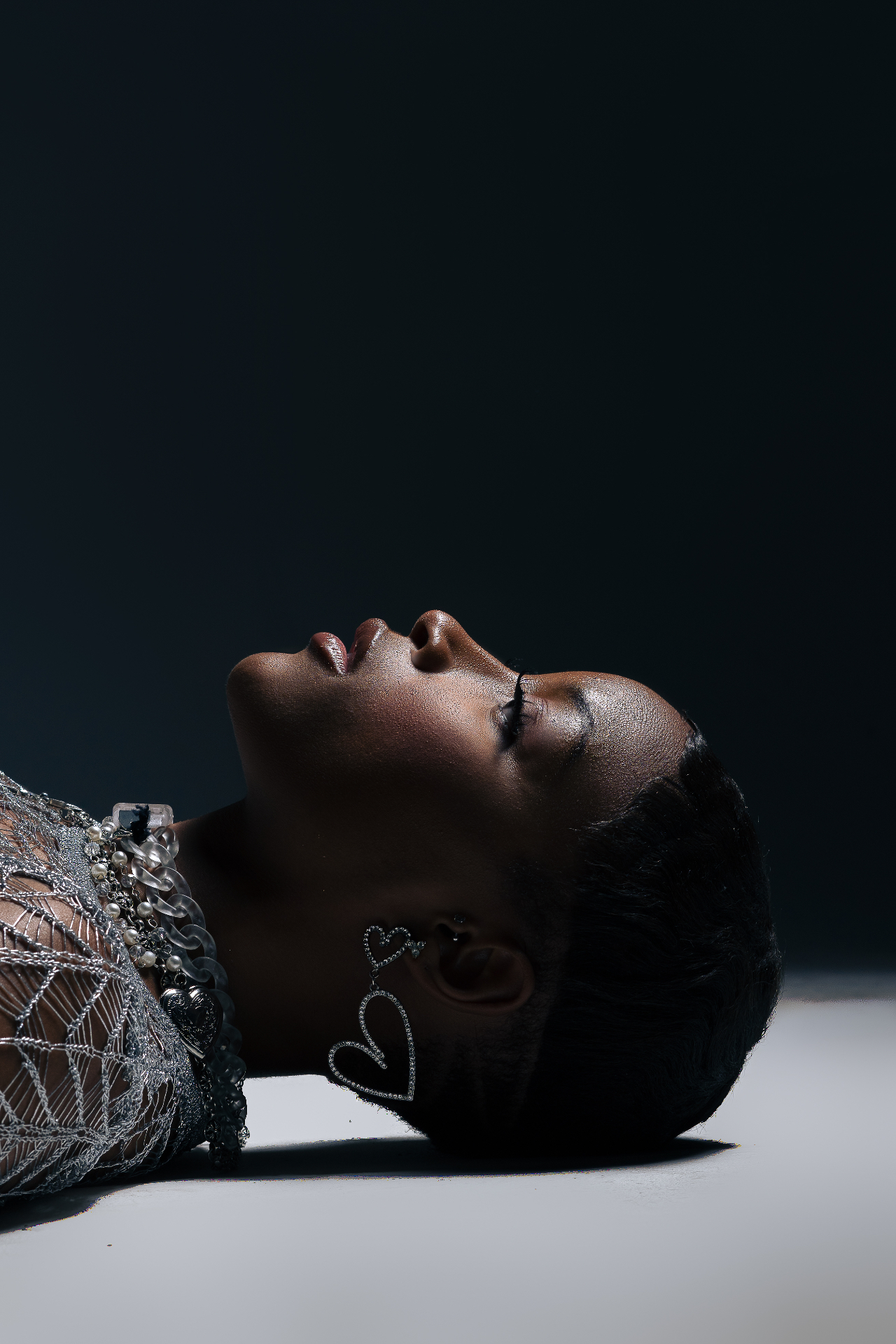Close-up profile beauty shot in silver mesh and a pearl chain against a dark backdrop