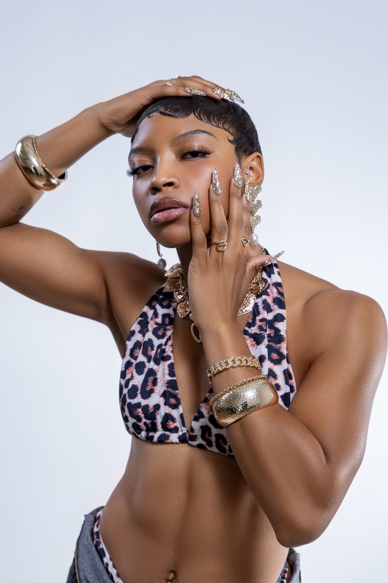 Studio beauty shot in a leopard-print halter top with gold jewelry, hand raised to the face