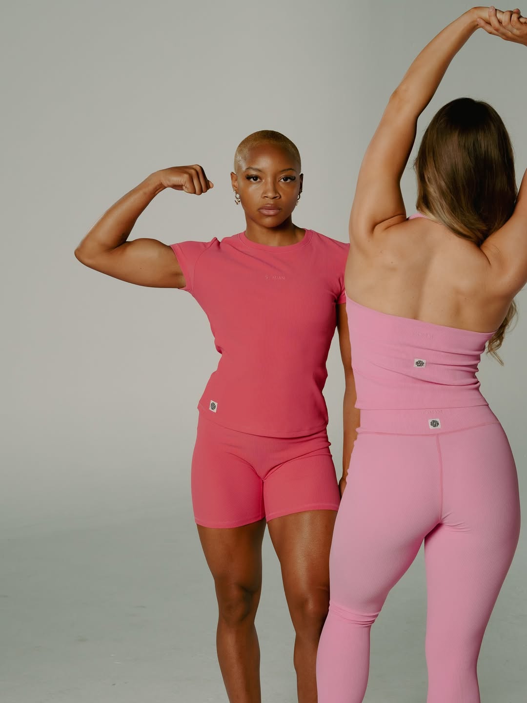 Three-quarter fitness shot flexing a bicep in a matching pink ribbed set
