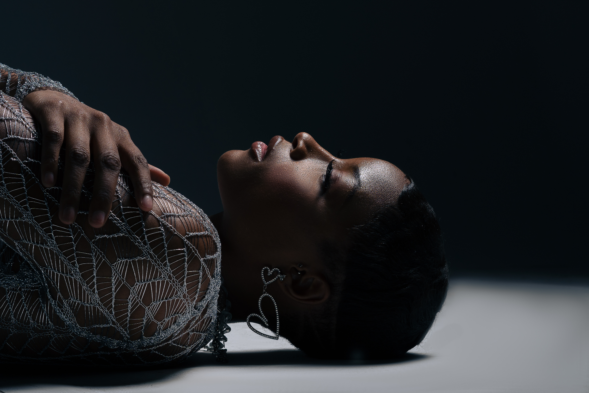 Close-up beauty shot in silver mesh with a hand resting on the chest against a dark backdrop