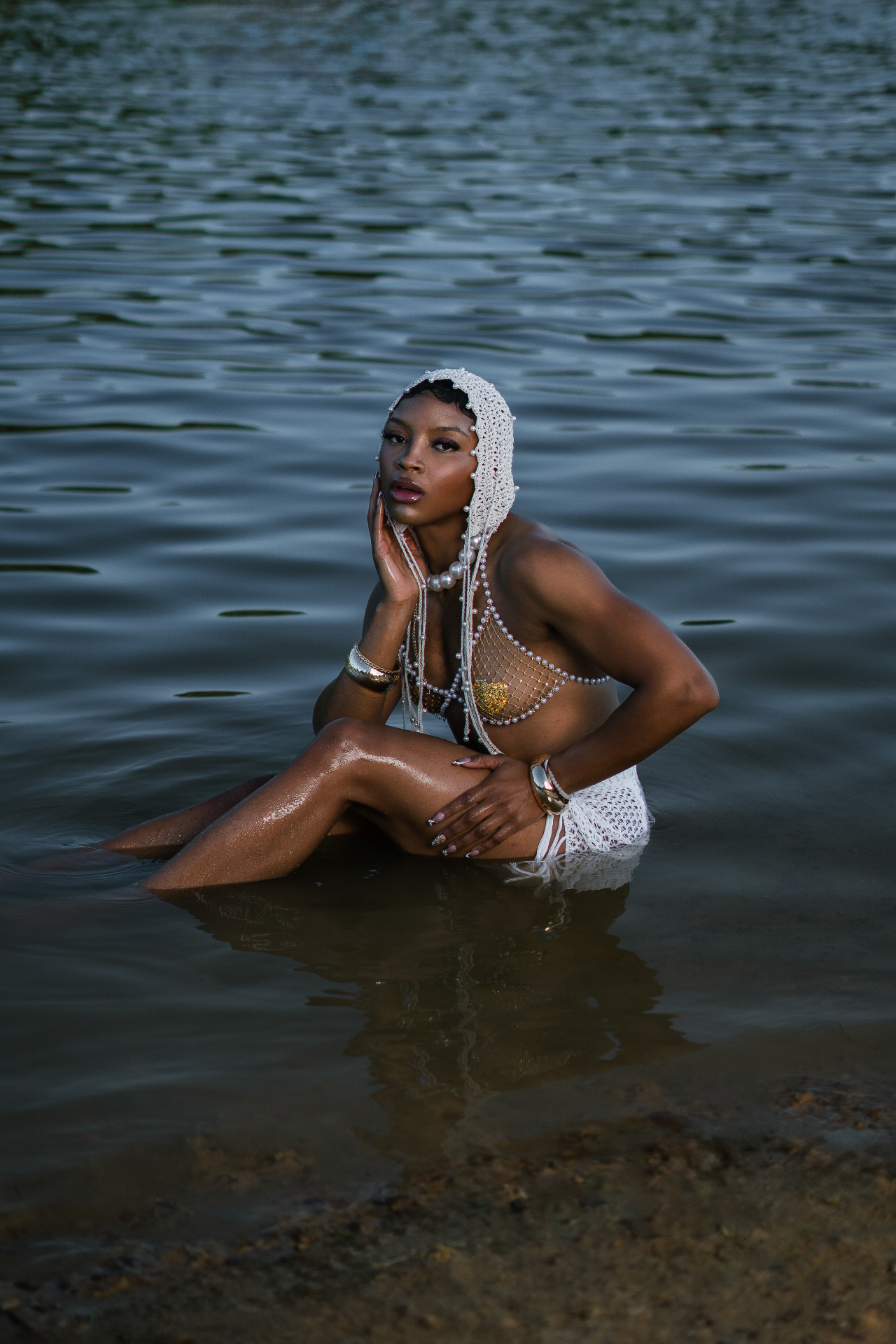 Full-length editorial shot in a pearl headpiece and pearl net top sitting in the water