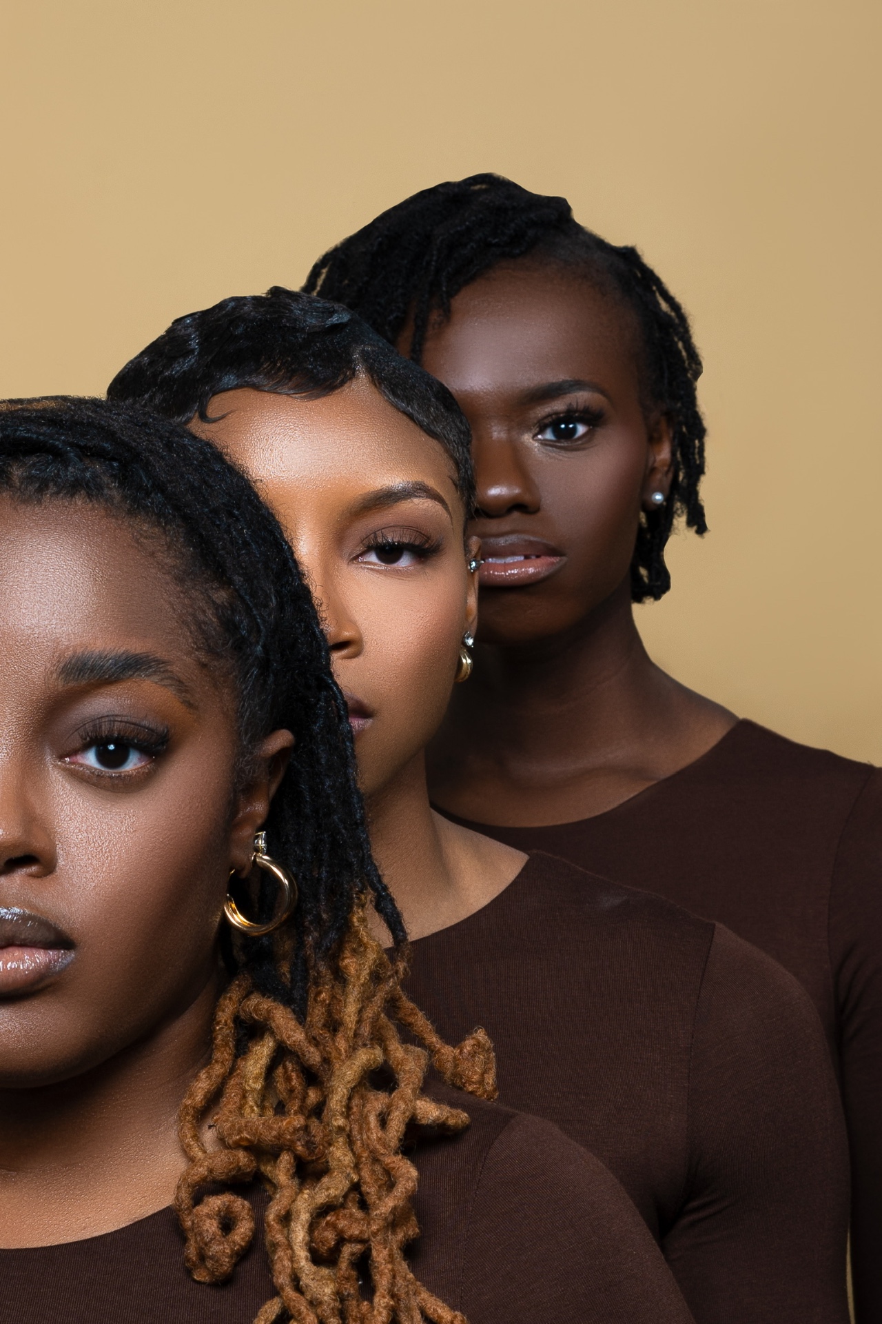 Beauty campaign portrait with three models in brown tops against a tan backdrop