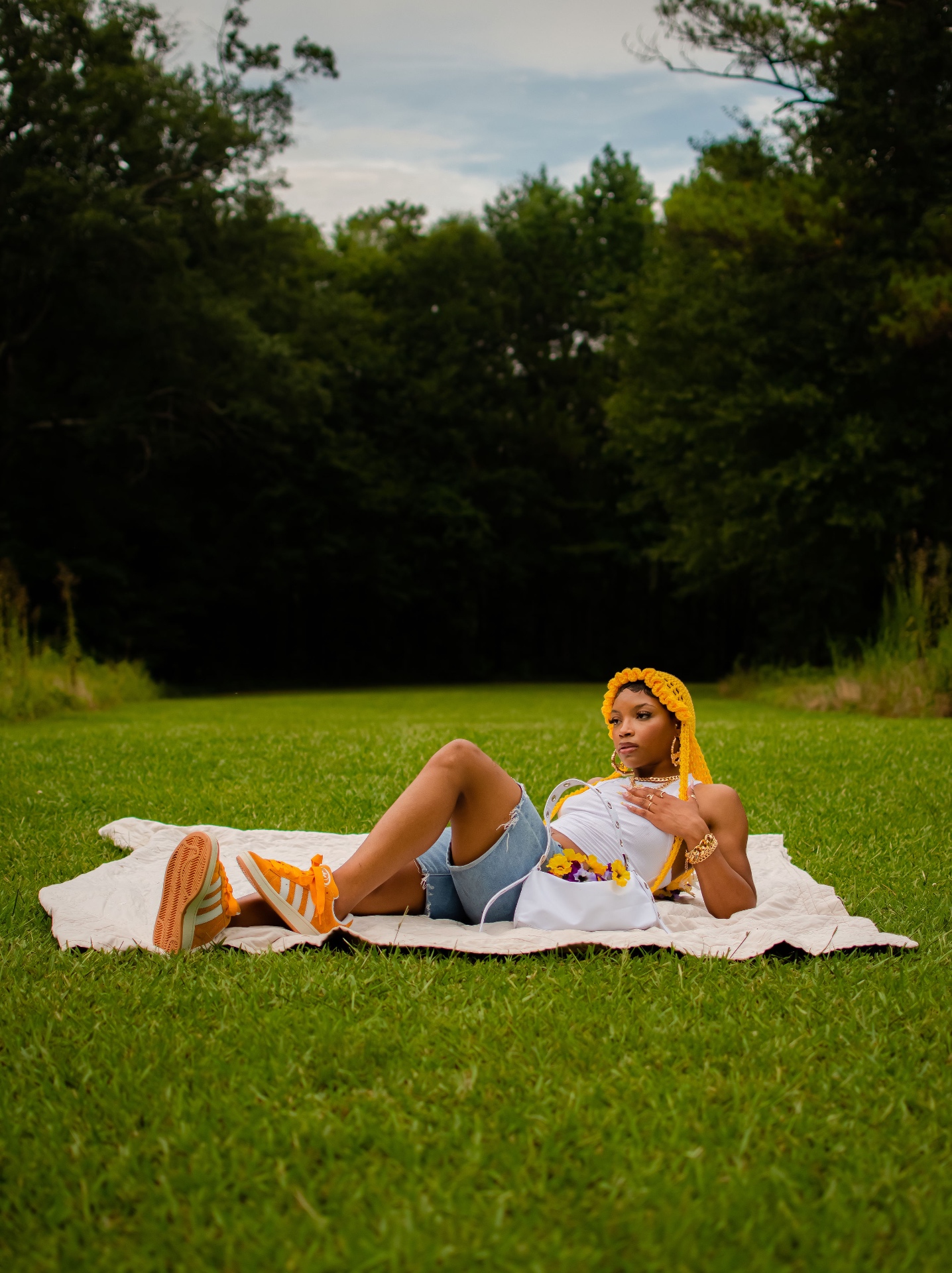 Editorial fashion shot in a yellow knitted headpiece and white tank lying on a blanket in the grass