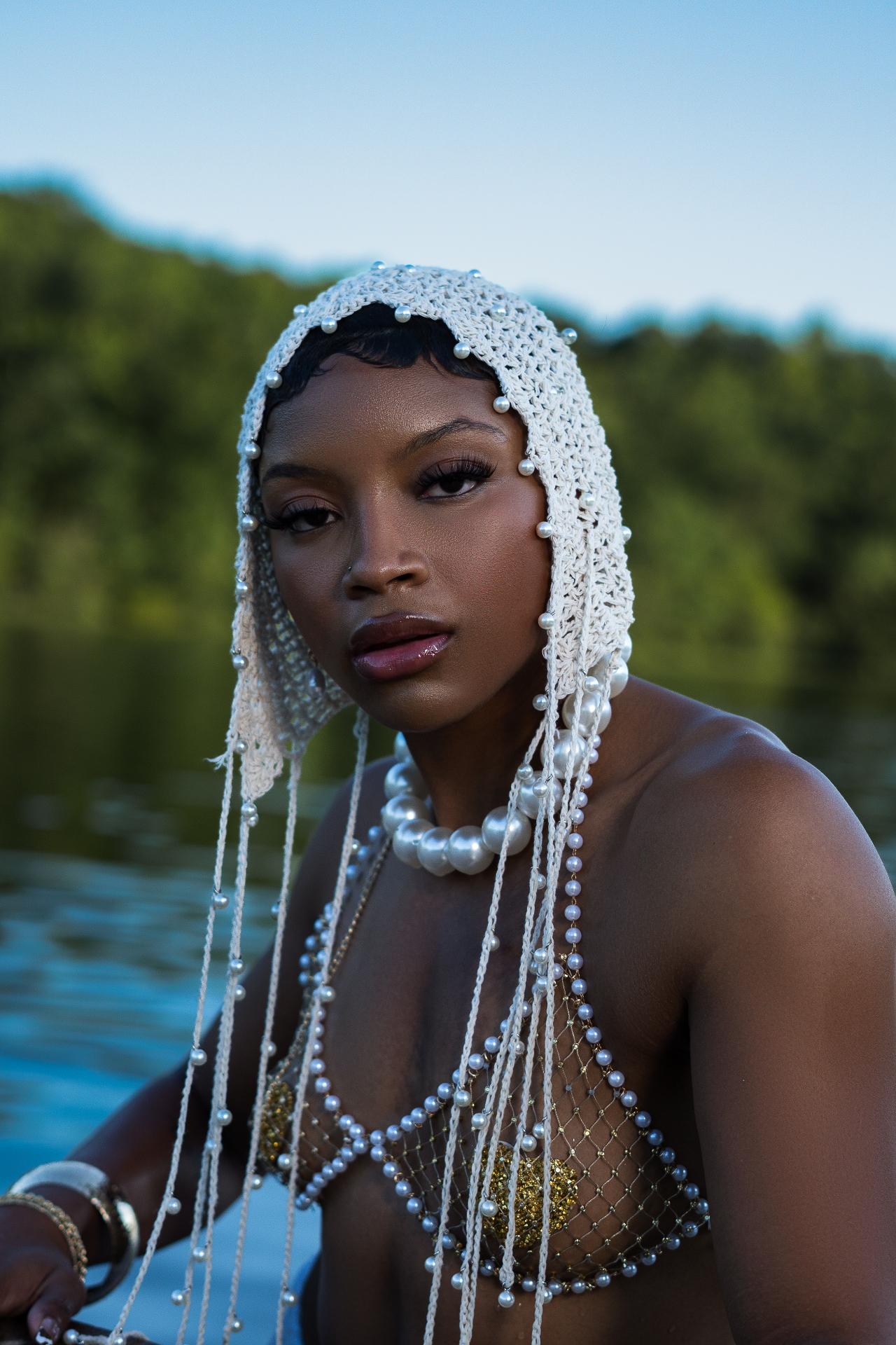 Close-up editorial shot in a pearl-studded knitted headpiece and pearl net top